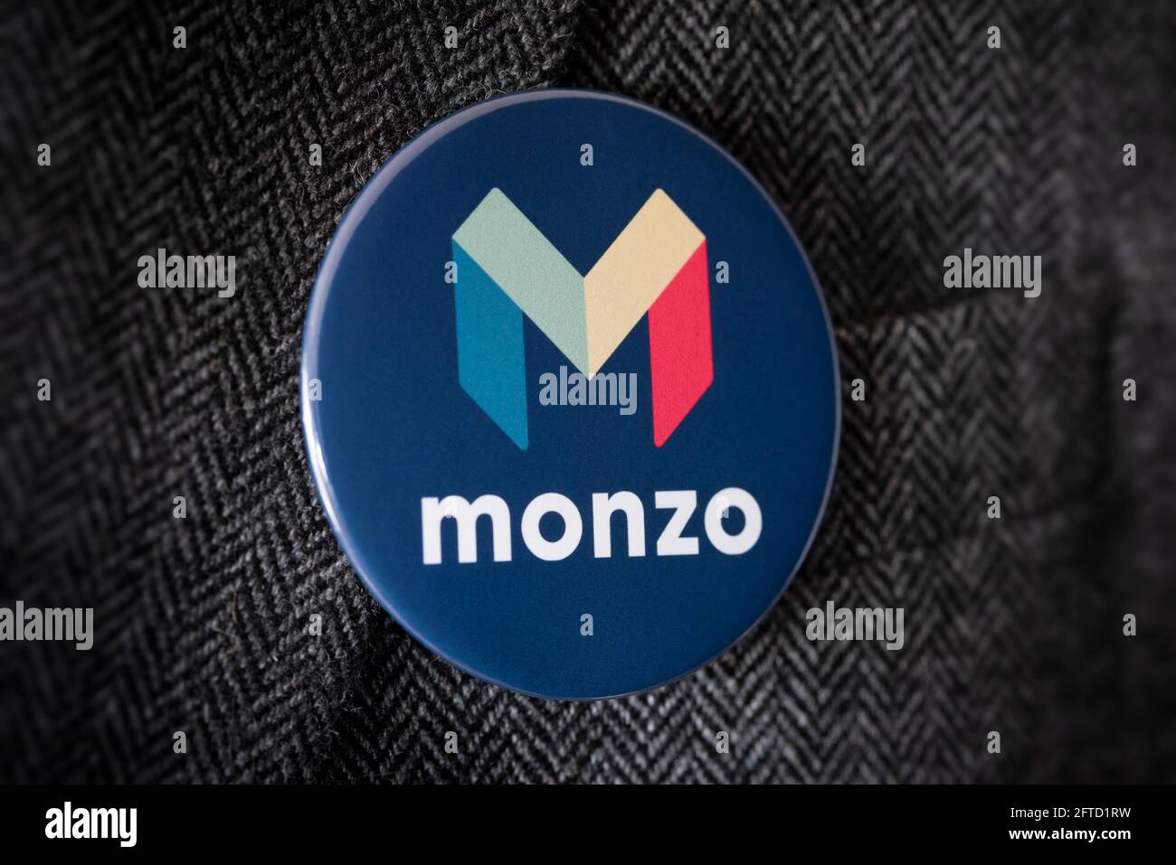 Ein Knopfabzeichen mit dem Logo von Monzo Bank, das an einer Anzugjacke befestigt ist. Stockfoto