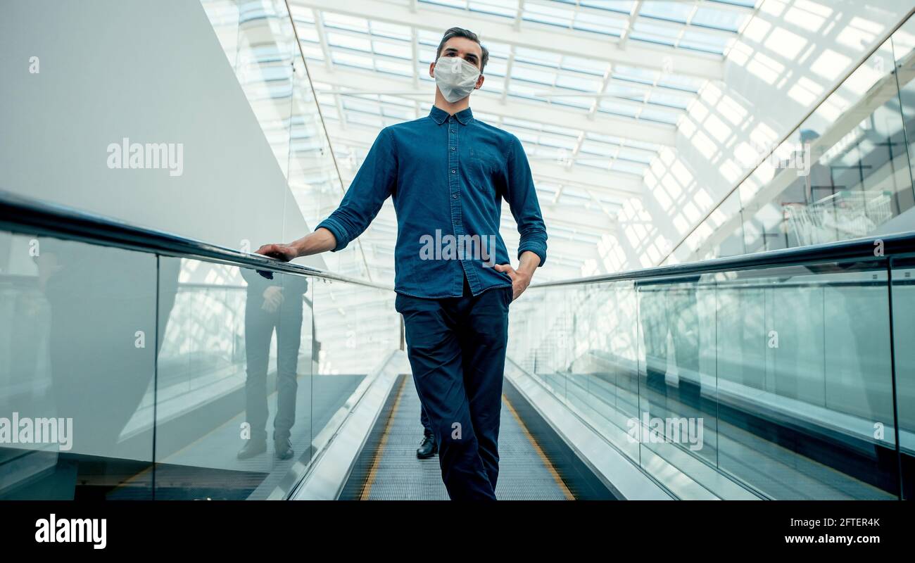 Junger Mann in einer Schutzmaske, der auf der Rolltreppe steht. Stockfoto