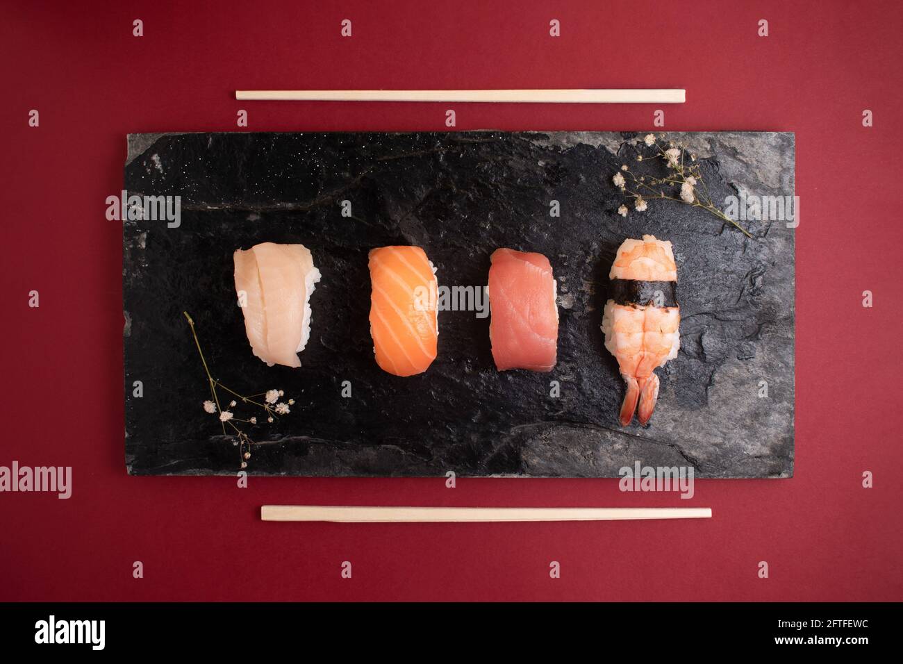 Draufsicht auf vier Arten von Sushi auf Steinplatte mit rotem Hintergrund und Sushi-Essstäbchen an den Seiten. Stockfoto