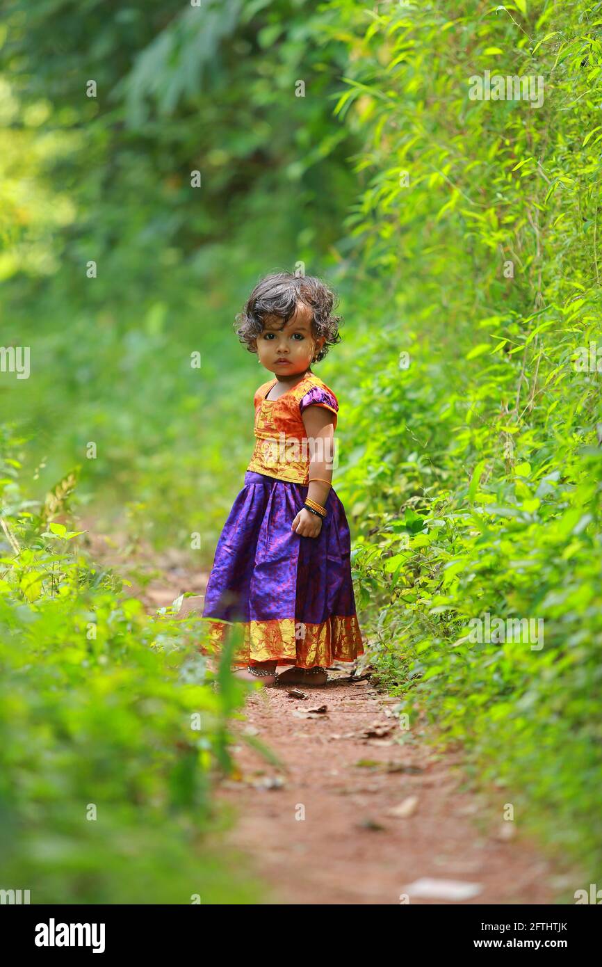 Südindische niedliche Mädchen Kind trägt schöne traditionelle Kleid langen Rock und Bluse, zu Fuß durch Dorf Weg mit viel Grün Hintergrund. Stockfoto