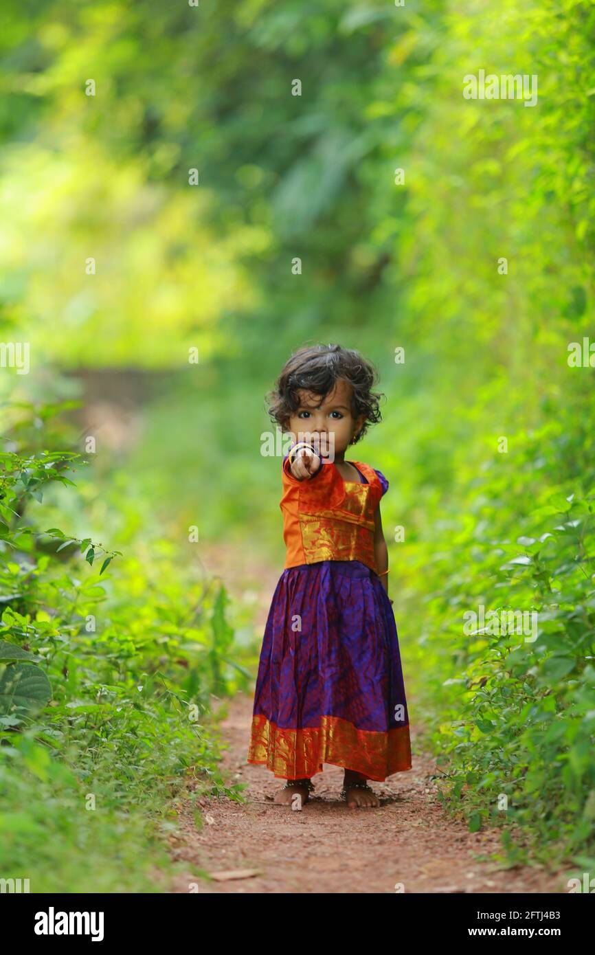 Südindische niedliche Mädchen Kind trägt schöne traditionelle Kleid langen Rock und Bluse, zu Fuß durch Dorf Weg mit viel Grün Hintergrund. Stockfoto