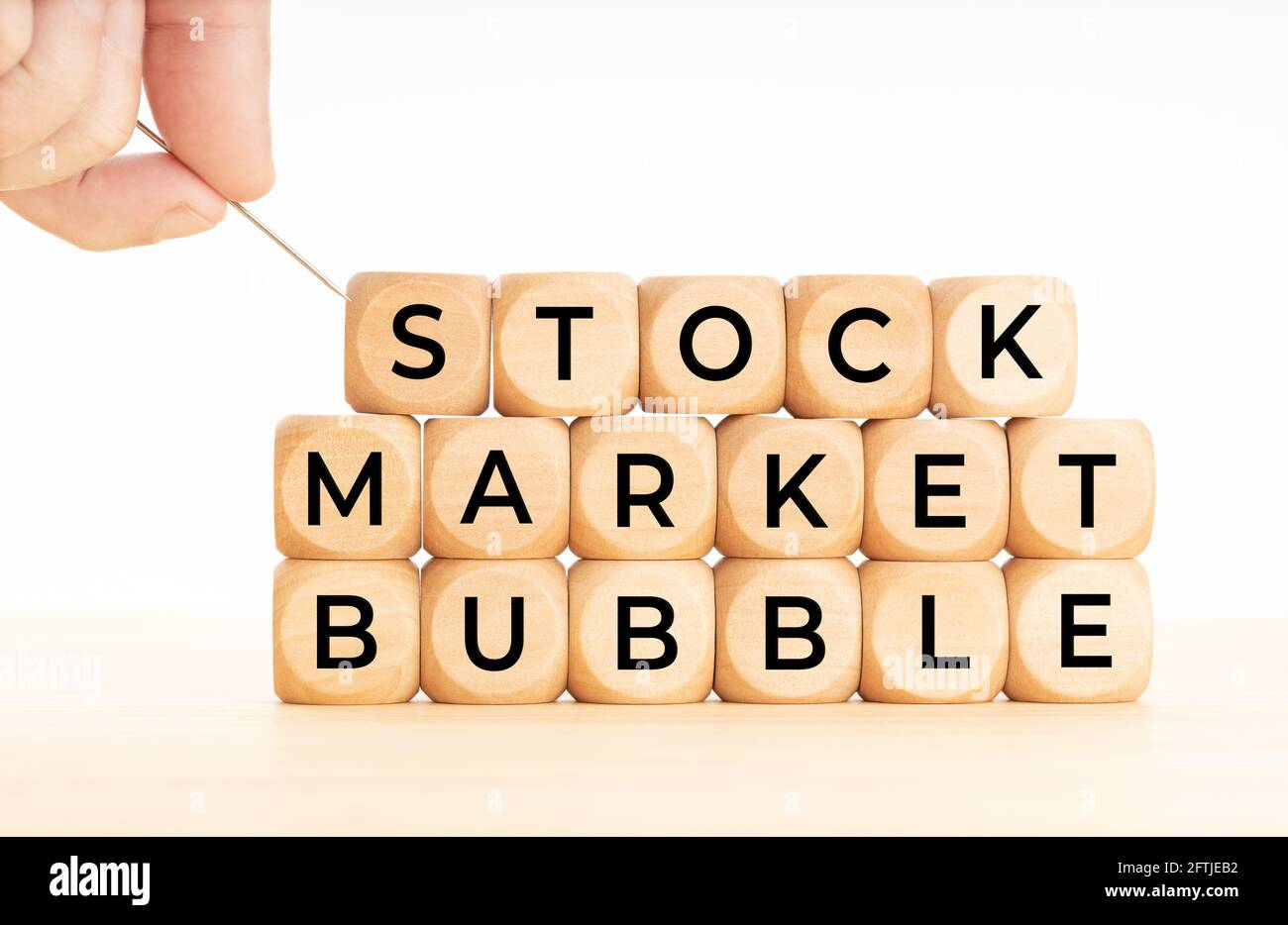 Hand hält eine Nadel bereit, um eine Blase an der Börse zu platzen, Wörter auf Holzblöcke. Finanzcrash-Konzept Stockfoto