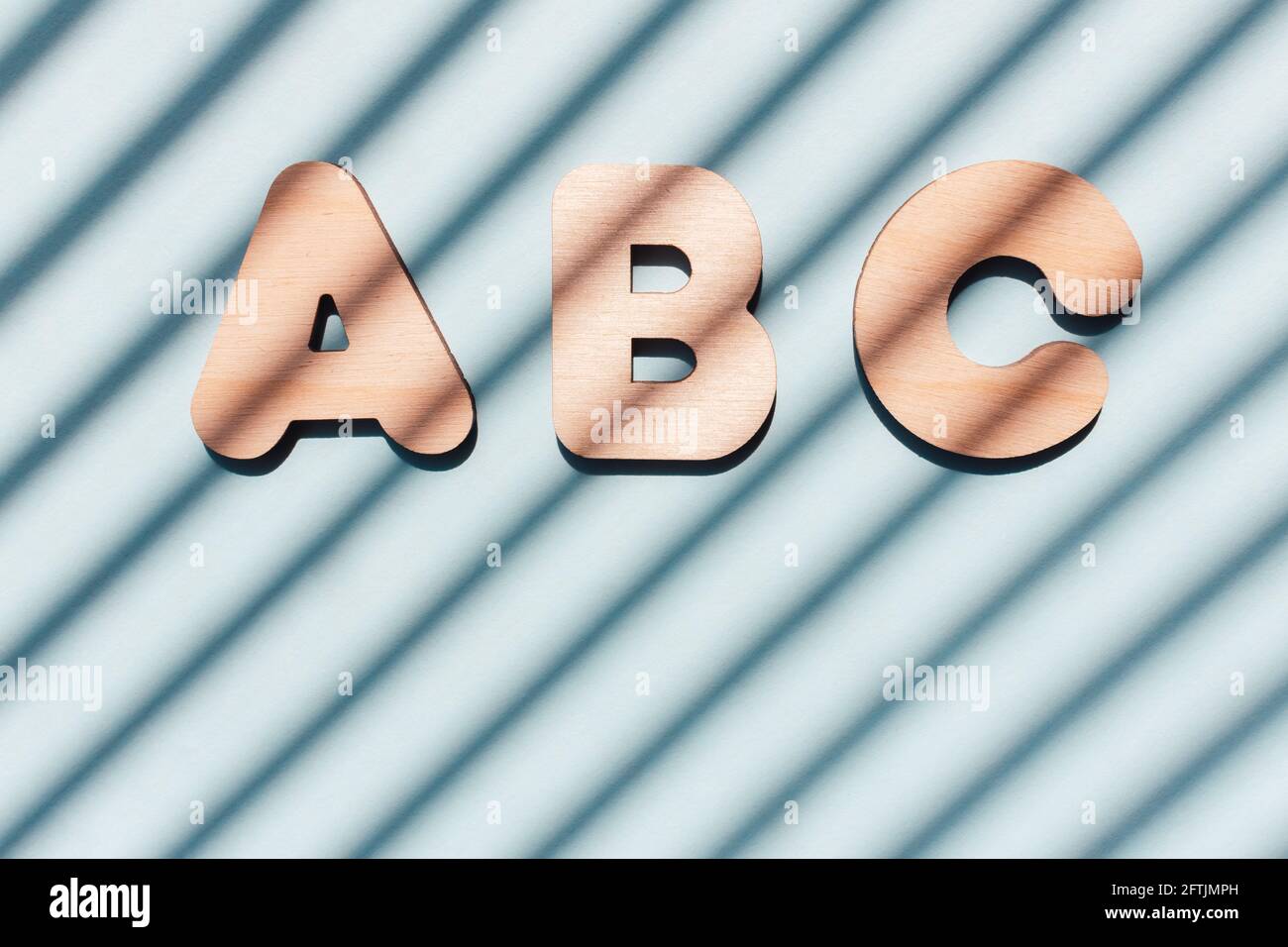 Inschrift ABC aus Holzbuchstaben. Das Konzept der Bedeutung von Bildung. Blauer Hintergrund mit diagonalen Schatten. Stockfoto