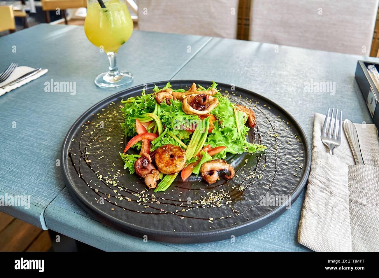 Frischer mediterraner Salat mit Garnelen, Tintenfisch und Tintenfisch auf einem schwarzen Teller auf der Veranda des Restaurants. Stockfoto