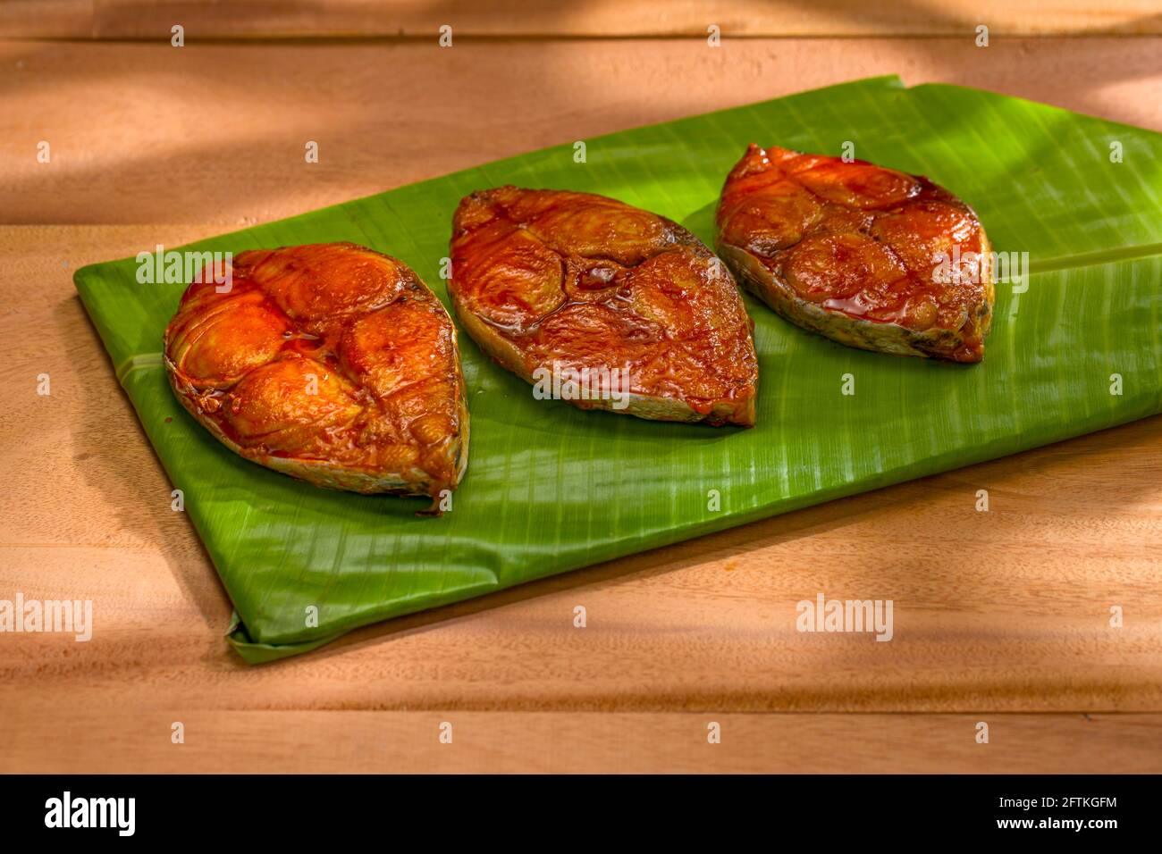 Seer Fish Fry schön auf Bananenblatt bedeckt Basis, die auf Holz strukturierten Hintergrund mit abstrakten Schatten auf dem Hintergrund platziert angeordnet ist. Stockfoto