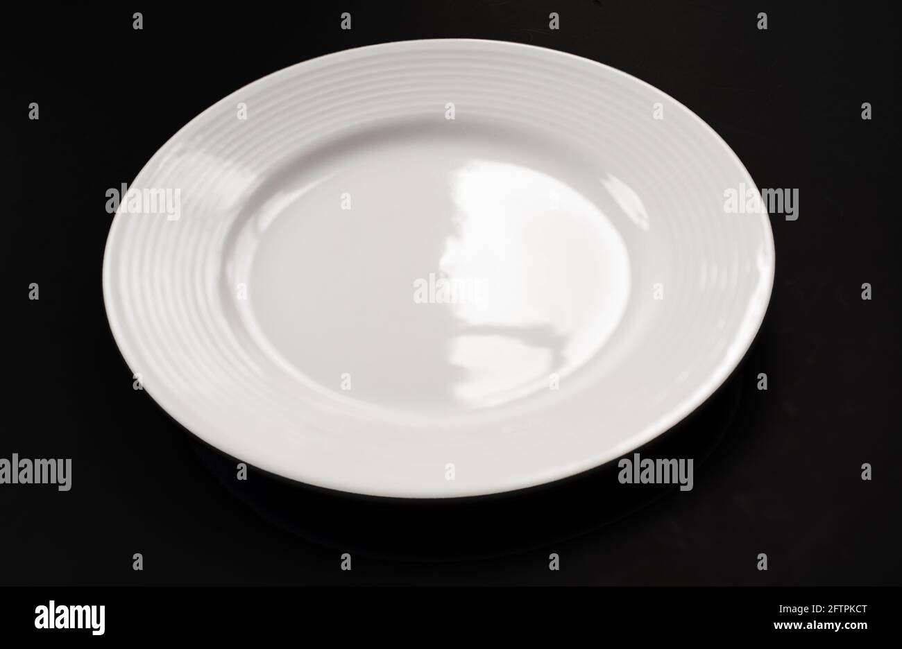 Eine weiße Platte auf schwarzem Hintergrund Nahaufnahme. Diese leere Schale aus sauberem weißem Glas ist ein Glasoobjekt mit Lichtreflektion ohne Nahrung. Stockfoto