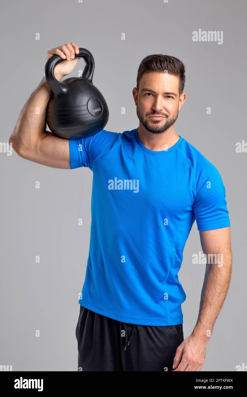 Junge sportliche fit 30er kaukasischen Mann posiert mit Kettlebell auf Grauer Hintergrund Stockfoto