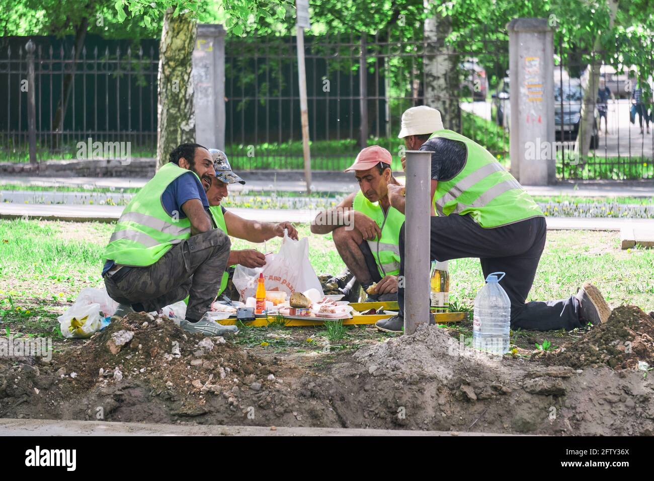 Perm, Russland - 18. Mai 2021: Brigade von Straßengastarbeitern essen während einer Pause auf der Straße zu Mittag Stockfoto