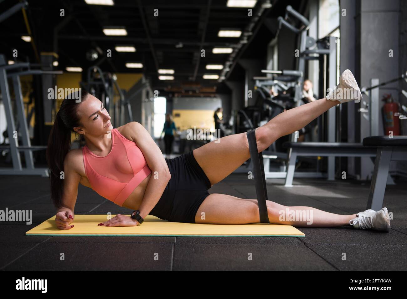 Junge Fitness-Frau tut Widerstand Band Bein hebt an der Fitnessraum Stockfoto