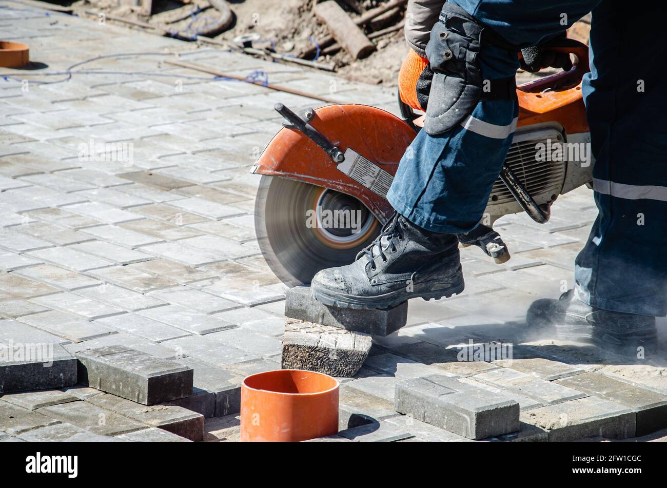 Ein Arbeiter schneidet Pflasterplatten mit einem Gasschneider und Eine Handsäge Stockfoto