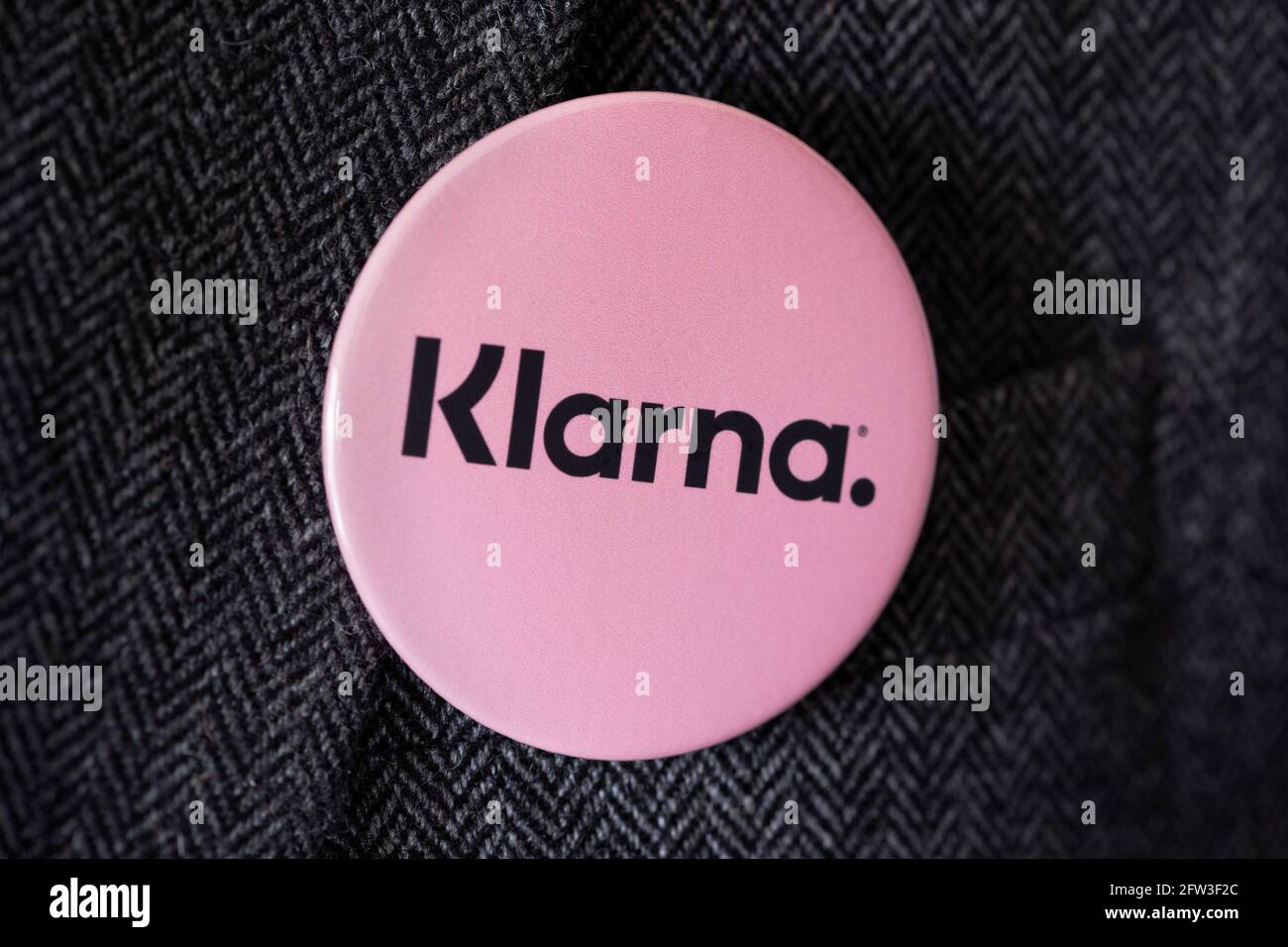 Ein Knopfabzeichen mit dem Logo von Klarna, das an einer Anzugjacke befestigt ist. Stockfoto