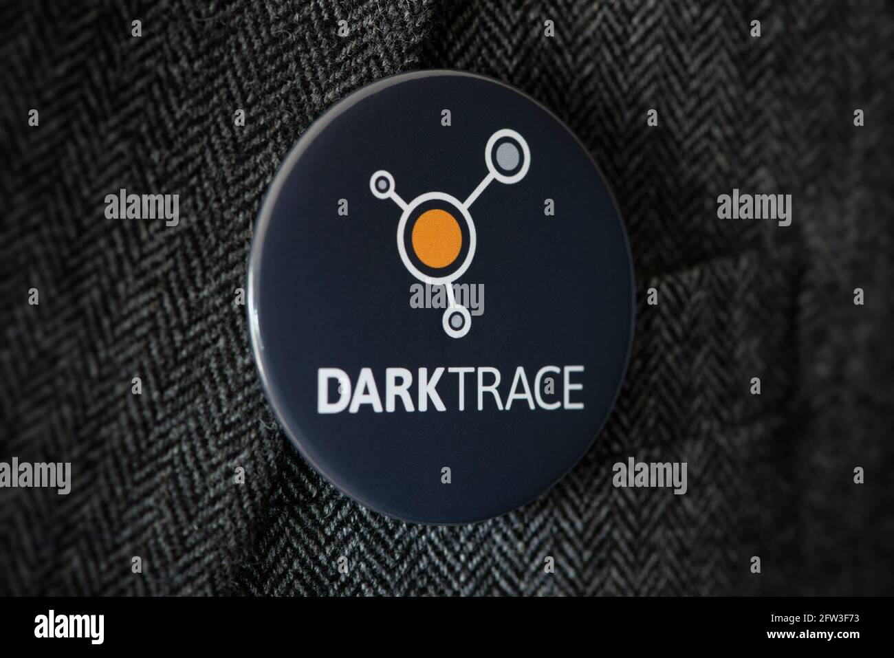 Ein Knopfabzeichen mit dem Logo der Cyber-Sicherheitsfirma Darktrace, das an einer Jacke befestigt ist. Stockfoto