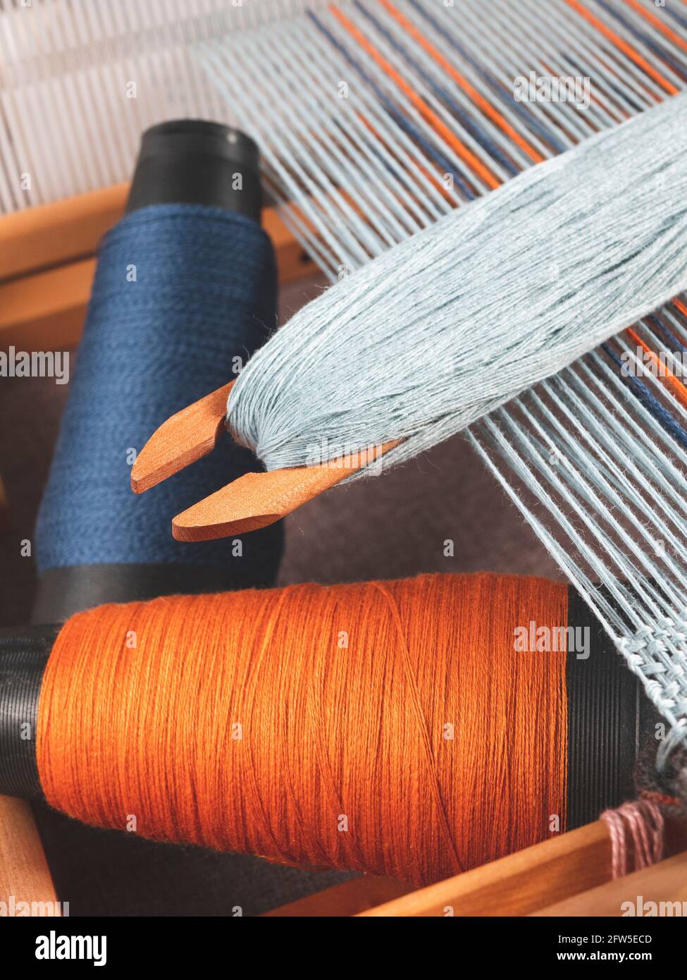 Shuttle mit blauem Faden und zwei Spulen mit Indigo- und Orangengarnen zum Weben von gestreiftem Textil, aufrechtes Format Stockfoto