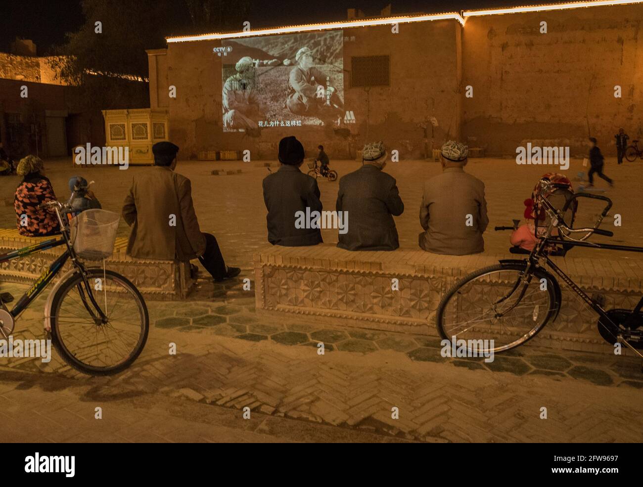 Uyhgur Männer sitzen auf einem kleinen Platz und schauen sich einen Propagandafilm über die Chinesische Revolution an. Kashgar , Volksrepublik China 2019 Stockfoto