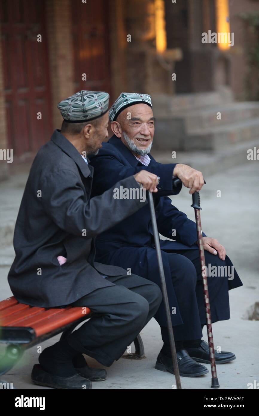 Zwei alte Männer sitzen mit Spazierstöcken und unterhalten sich auf einer Kashgar-Straße Kashgar, Xinkiang, Volksrepublik China, 2019 Stockfoto