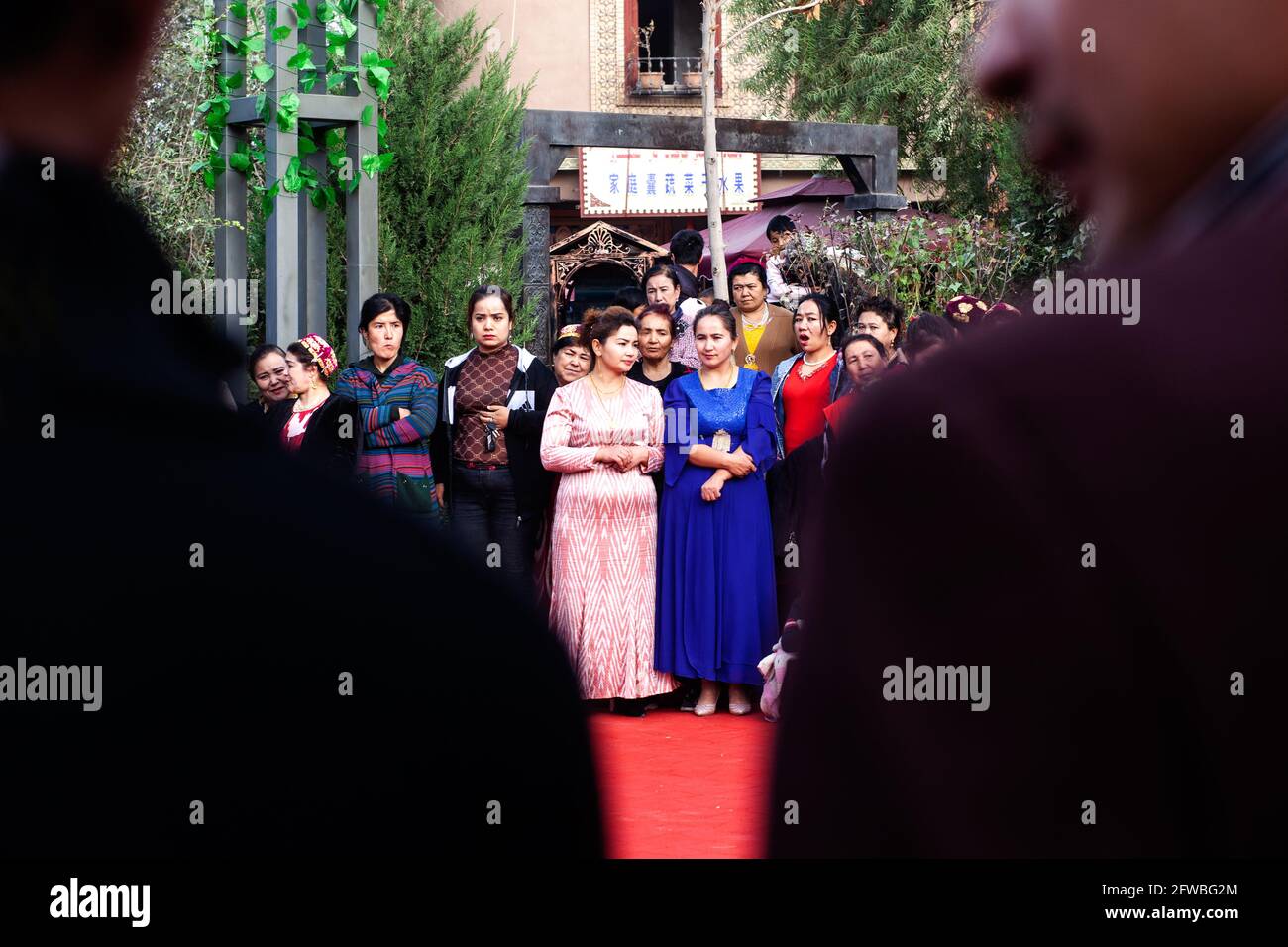 89 / 5000 in der Silhouette zweier Männer sehen wir eine Gruppe von Frauen der uigurischen Volksgruppe, die zu einer Feier gekleidet sind Kashgar, Xinkiang, P Stockfoto