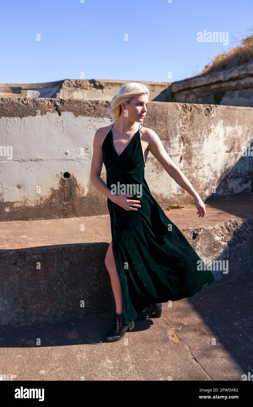 Mode an ungewöhnlichen Orten, Frau in langen Kleidern steht in Ruinen von Waffenbatterien | Kleid bläst im Wind Stockfoto