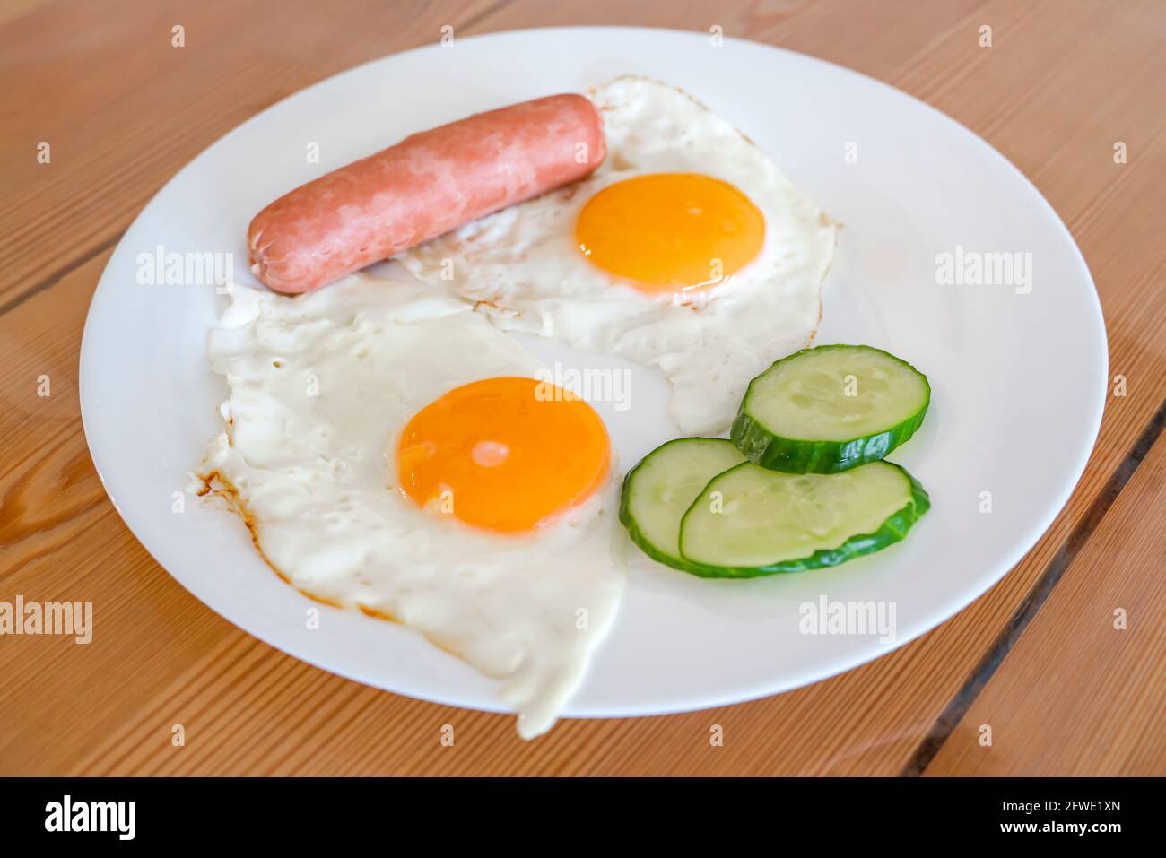 Spiegeleier aus zwei Eiern mit Gurken und Wurst zum Frühstück. Spiegeleier, Sonnenseite auf einem Teller. Gesundes Lebensmittelkonzept. Stockfoto