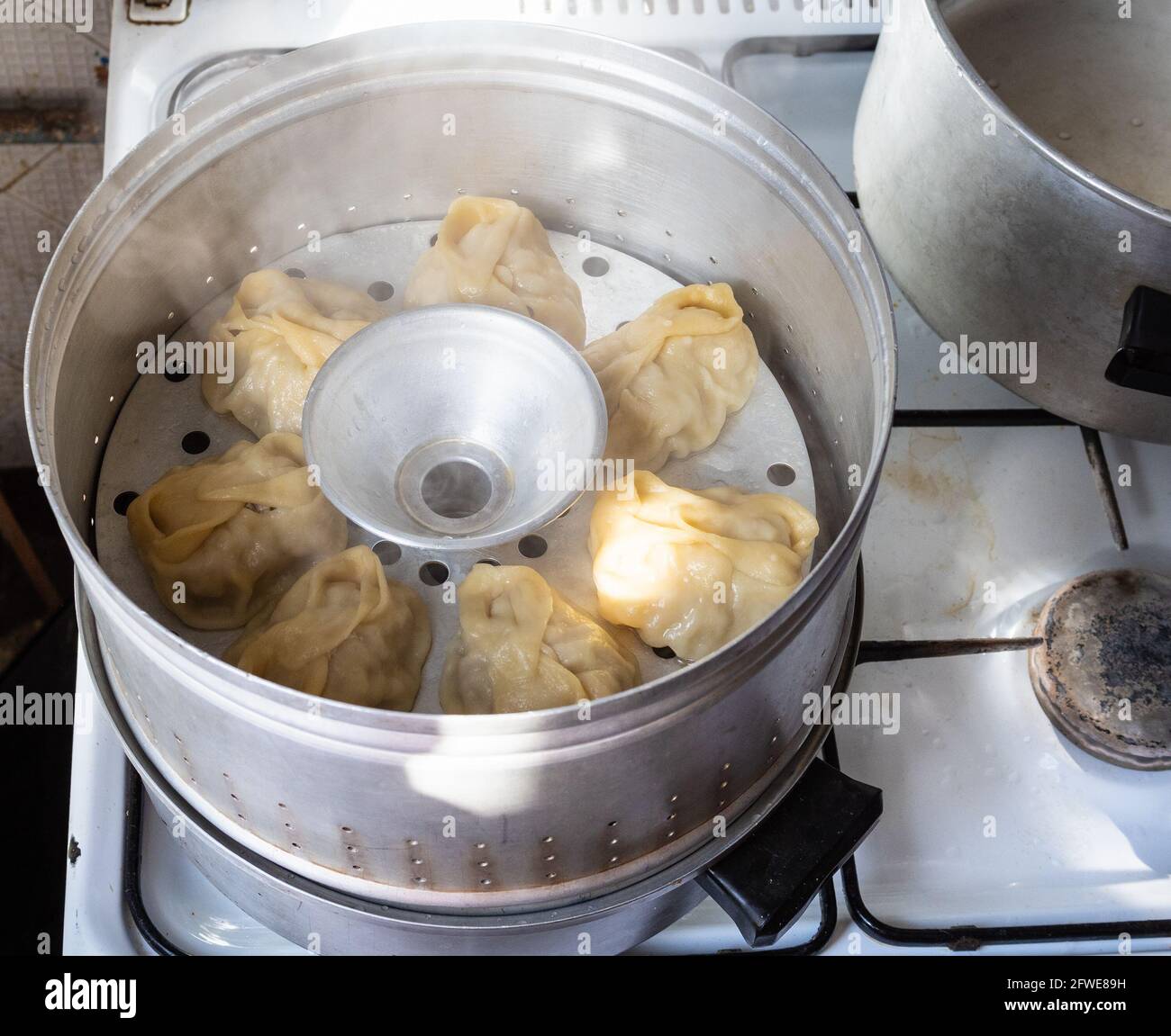 Hausgemachte Manti kochen in Aluminium-Dampfgarer auf dem Herd in Wohnküche Stockfoto