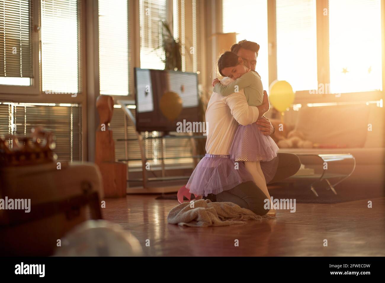 Ein junger Vater und seine kleine Tochter umarmen sich, während sie zu Hause in wunderschöner Atmosphäre ein Balletttraining machen. Familie, zusammen, zu Hause Stockfoto