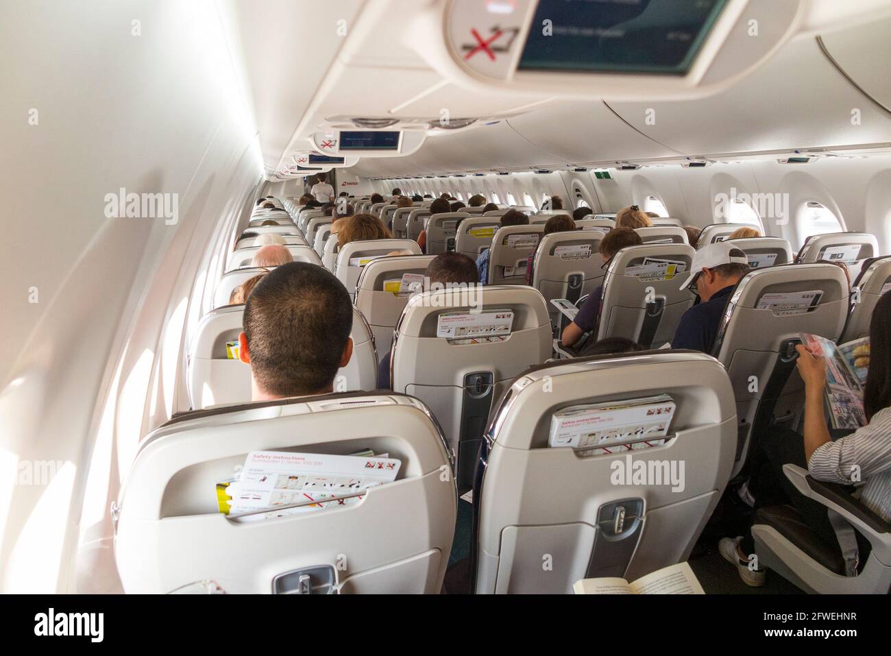 Der Kabinenggang mit Sitzlehnen und Passagieren von hinten gesehen auf einem Flugzeug/Flugzeug/Flugzeug der Bombardier C-Serie (ein Flugzeug, das jetzt als Airbus A220 vermarktet wird). (100) Stockfoto