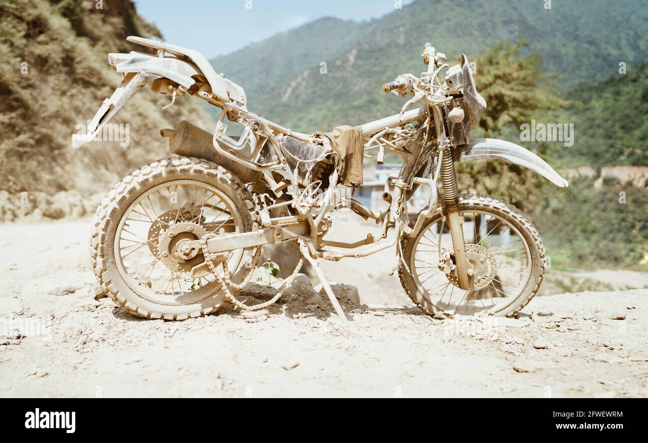 Verlassene alte Motocross-Motorräder werden in tiefem Straßenstaub in der Nähe der überfüllten Stadtstraße in Ramechhap, Nepal, ertränkt. Stockfoto