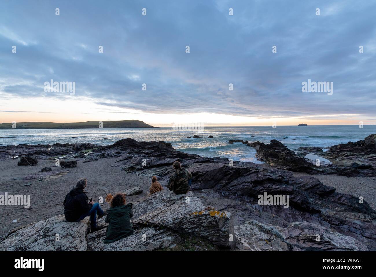 4 Personen und ein Hund sitzen und beobachten den Sonnenuntergang am Greenaway Beach North Cornwall. Stockfoto