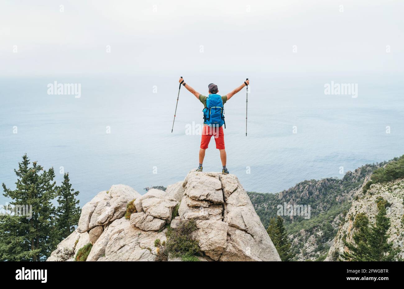 Junge Wanderer Backpacker Mann Rose Trekking Stöcke bis genießen die Mittelmeer auf der Klippe während des Lykischen Wanderwegespaziergangs.berühmte Likya Yolu Türkisch Stockfoto
