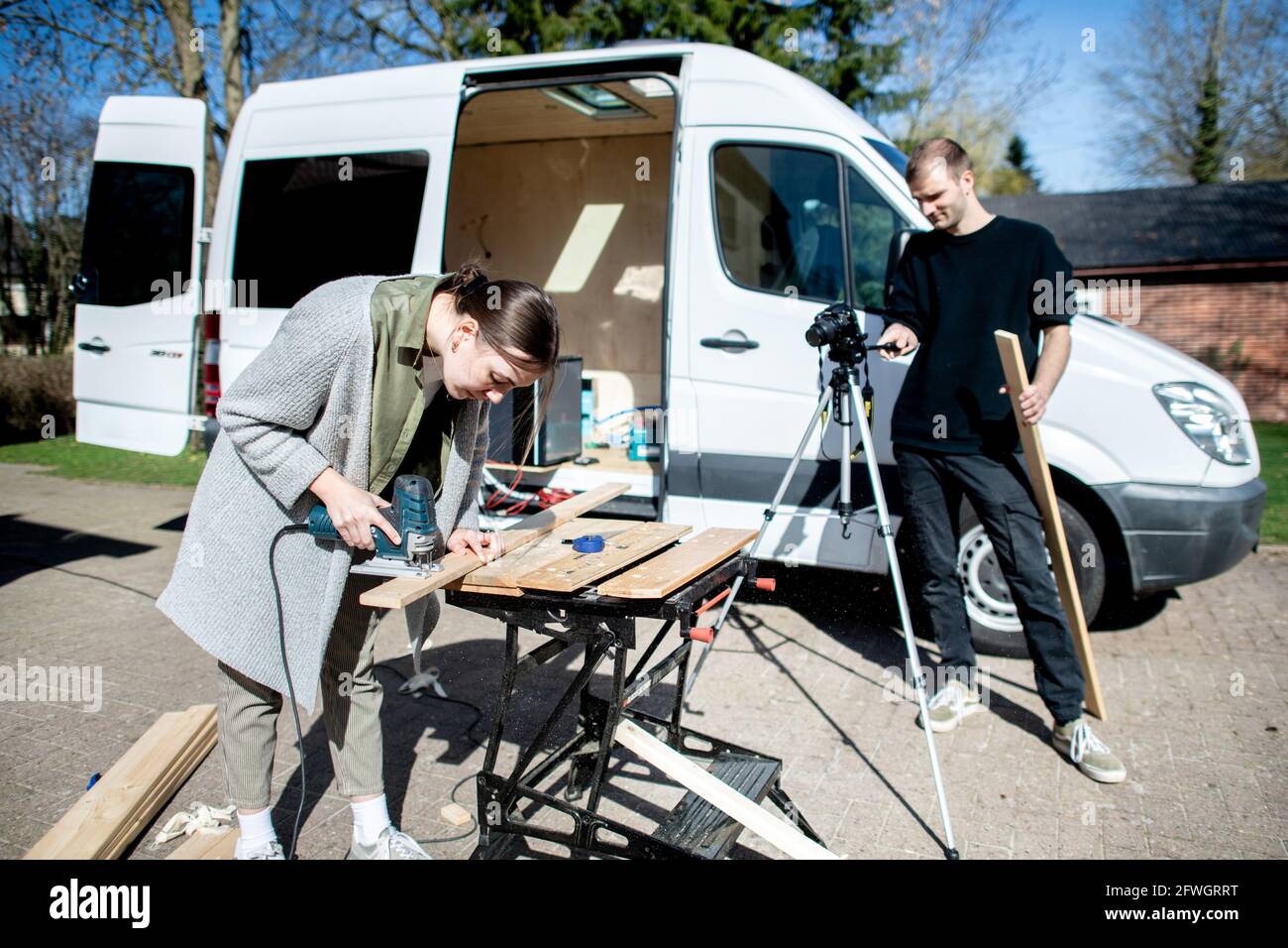 03. April 2021, Niedersachsen, Großenmeer: Greta Thomas und Hannes Wehrmann schneiden Holz vor ihrem Mercedes-Benz Sprinter, den das Paar mit eigener Arbeit in einen Wohnmobil umwandelt. Ferien mit einem selbst gebauten Wohnmobil sind im Trend - die Umsetzung wird oft ausführlich für YouTube oder Instagram dokumentiert. Foto: Hauke-Christian Dittrich/dpa Stockfoto