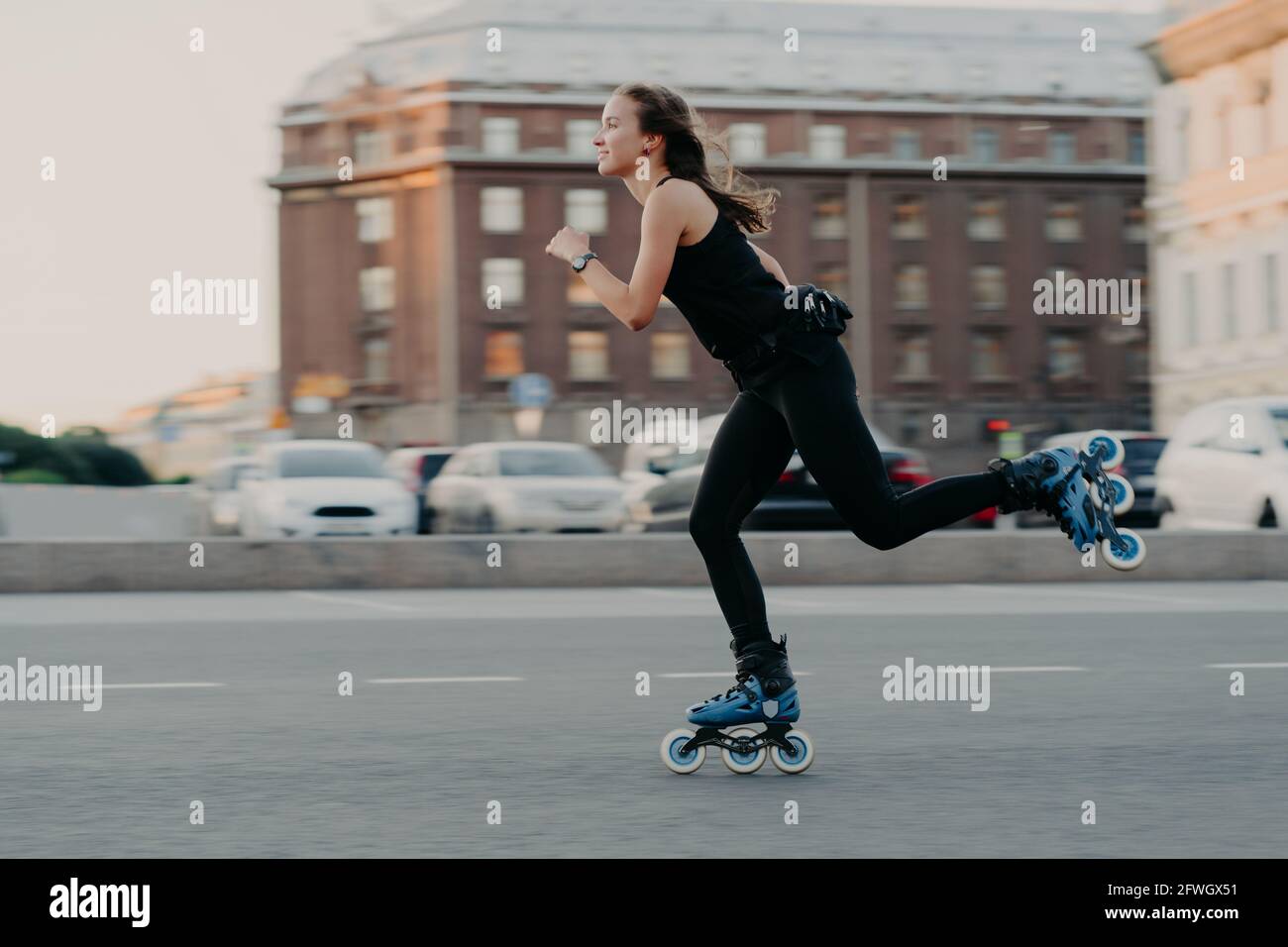 Frau reitet auf Rollen bewegt sich sehr schnell gekleidet in aktiv Wear genießt Rollerblading in Action-Posen in Urban fotografiert Setzen Sie sich ein Stockfoto