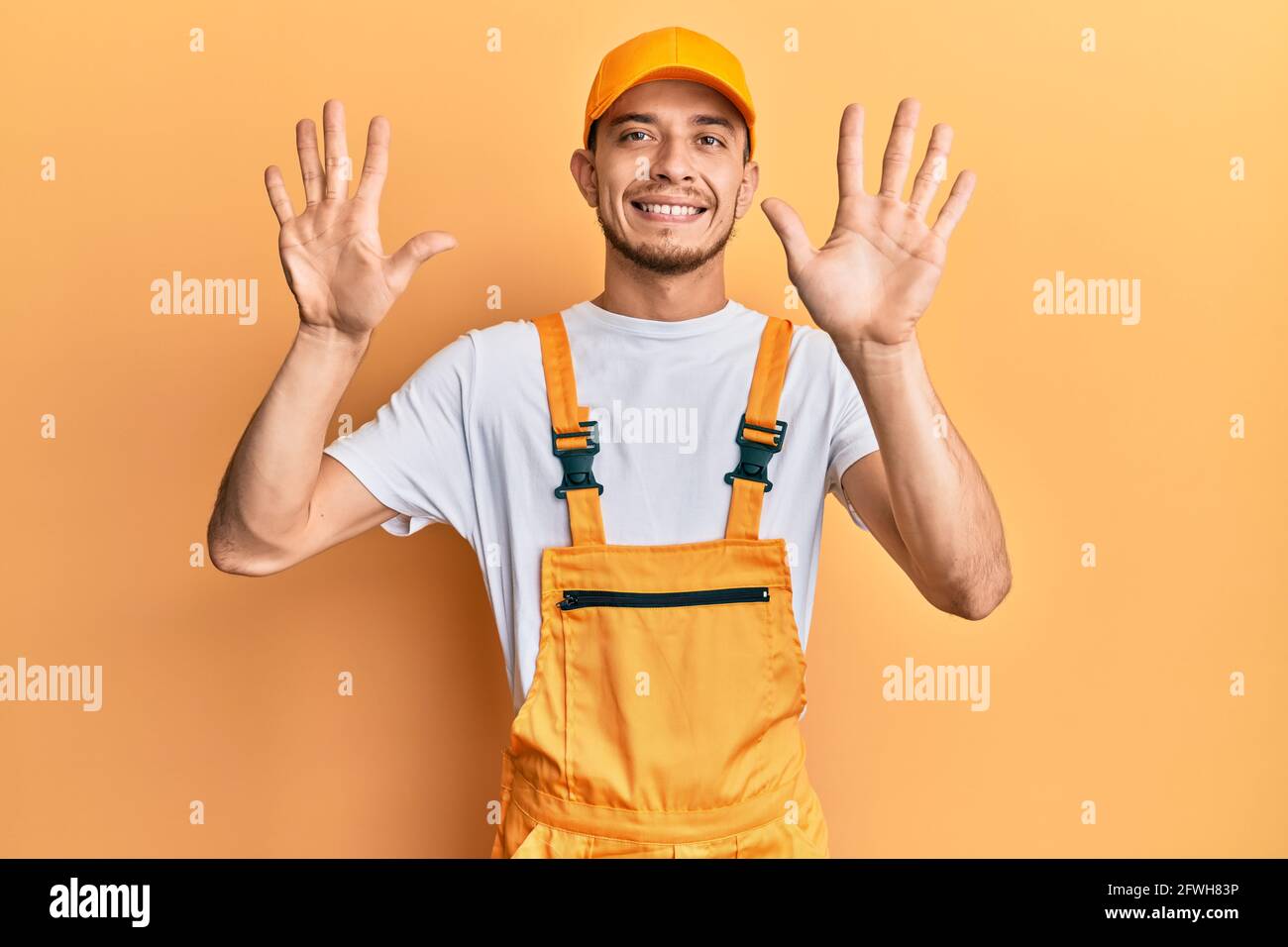 Hispanischer junger Mann in einer Handyman-Uniform, der mit den zehn Fingern nach oben zeigt und dabei selbstbewusst und glücklich lächelt. Stockfoto