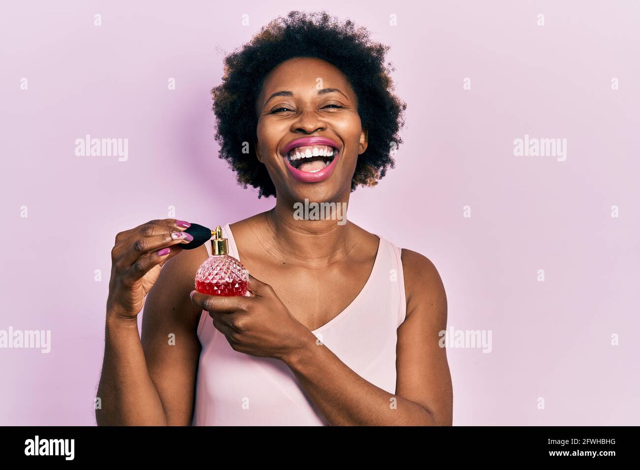 Junge afroamerikanische Frau hält Parfüm lächelnd und lacht laut, weil lustig verrückt Witz. Stockfoto