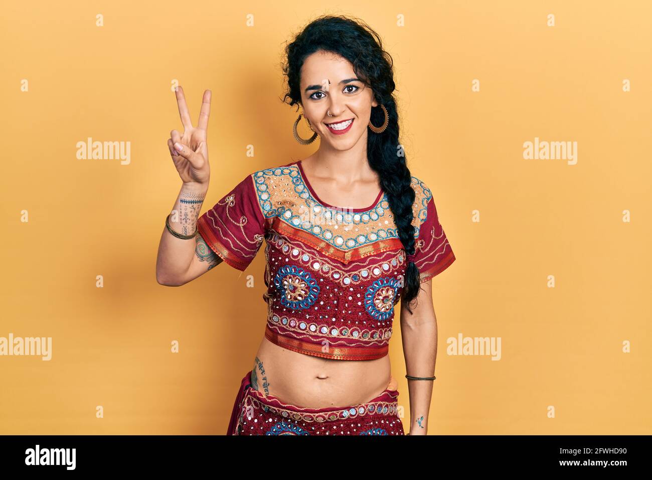 Junge Frau in Bindi- und bollywood-Kleidung zeigt und zeigt mit den Fingern Nummer zwei auf, während sie selbstbewusst und glücklich lächelt. Stockfoto