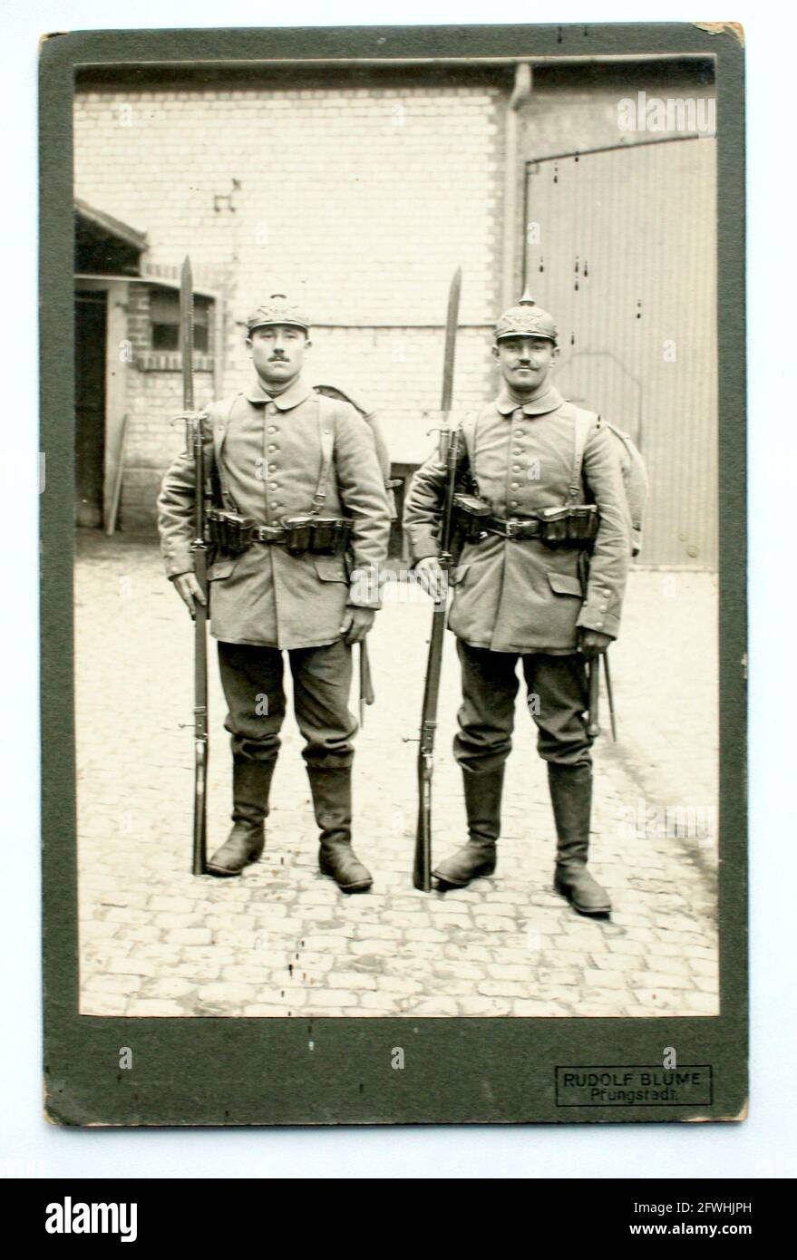 Zwei Soldaten in Felduniform, mit aufgepflanzenem Bajonett, Pickelhaube und Marschgepäck im Bauernhof, bereit für den Abmarsch in den Krieg um 1914. Stockfoto