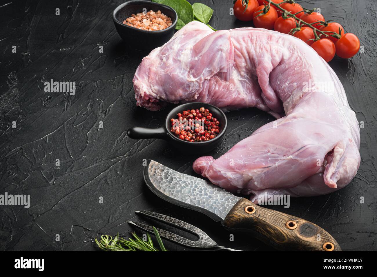 Rohes Kaninchenfleisch mit frischem Gemüse, Kräutern und Gewürzen, auf schwarzem Stein-Hintergrund, mit Platz für Text Stockfoto