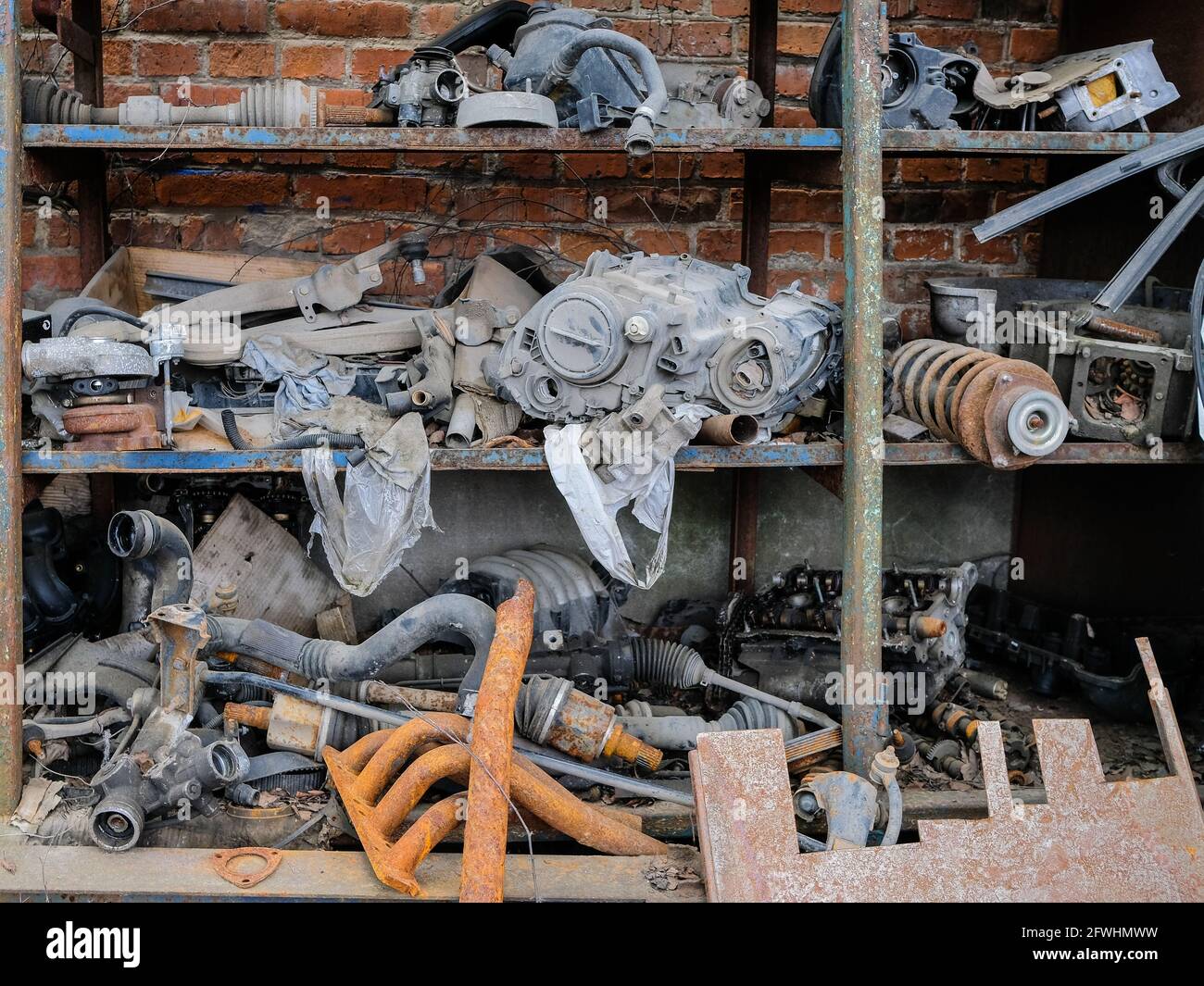 Alte rostige Autoteile stapelten sich auf einem Regal vor einem Backsteinwand-Hintergrund. Müll nach Autoreparaturen. Grunge. Stockfoto