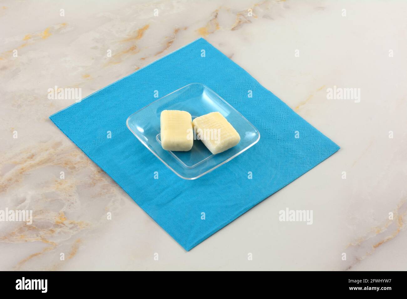 Zwei Mastix-Toffee-Bonbons in transparenter Bonbons-Schale Blaue Serviette auf dem Tisch Stockfoto