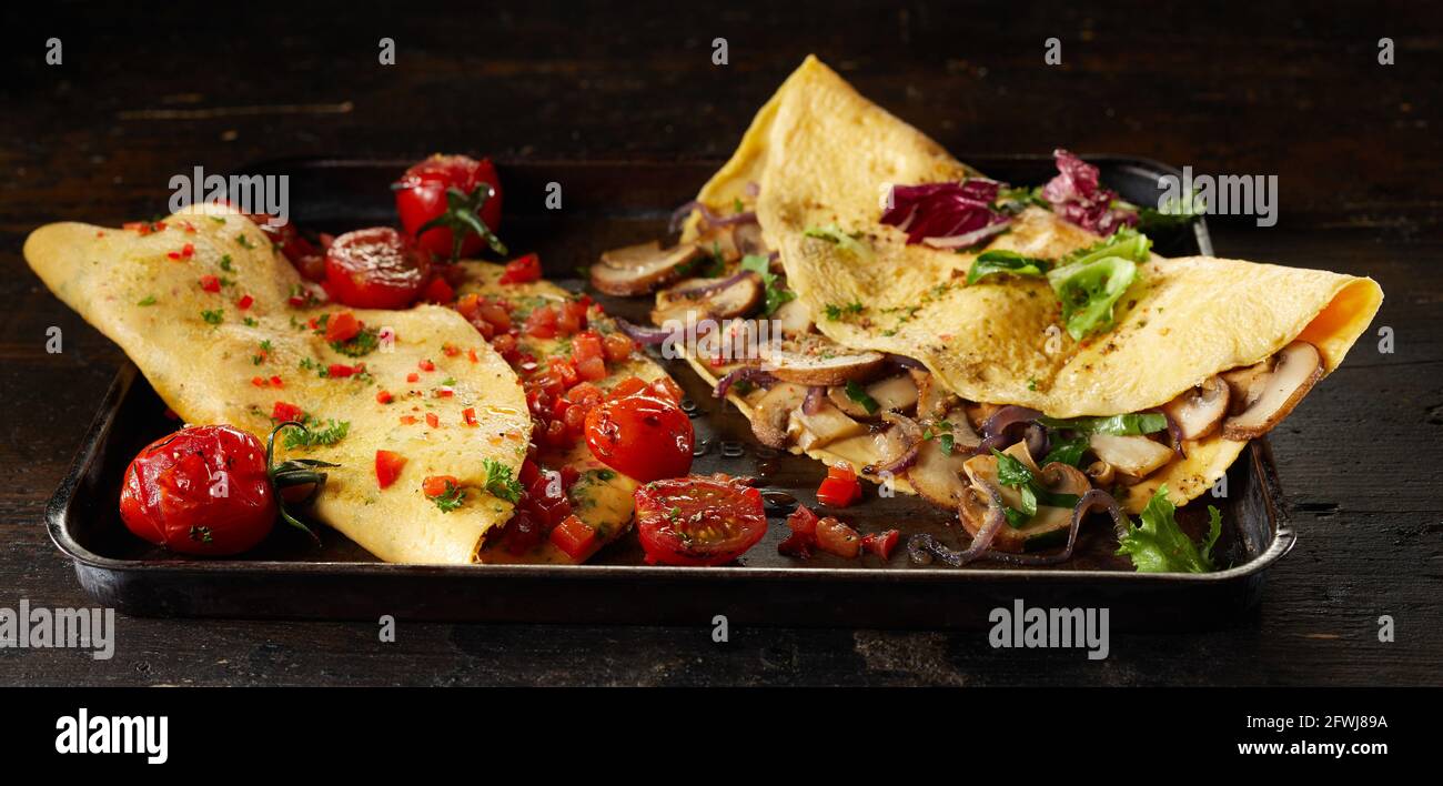 Appetitliche Omelettes mit Tomaten und Pilzen auf dem Tablett serviert Dunkler Tisch zum Mittagessen Stockfoto