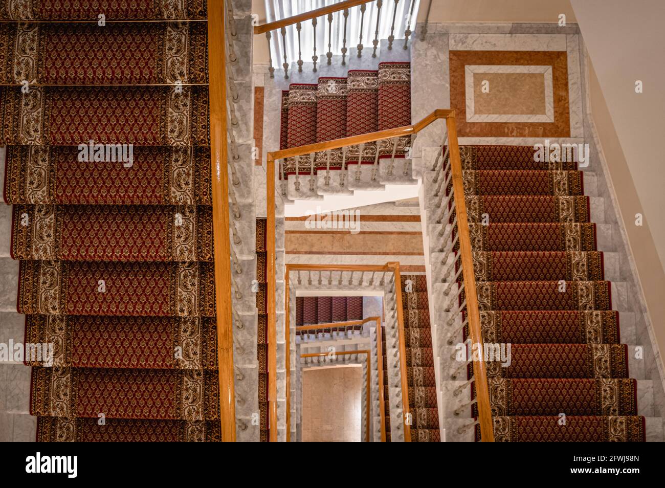 Blick nach unten auf eine Wendeltreppe mit mehreren mit Teppichen verzierten Flängen. Stockfoto