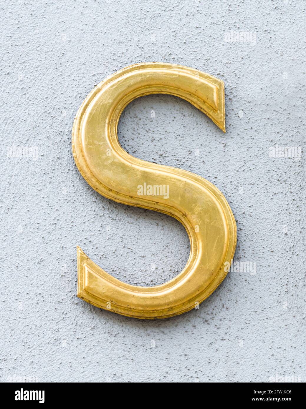 Goldener Buchstabe S auf einer hellgrauen Wand Stockfoto