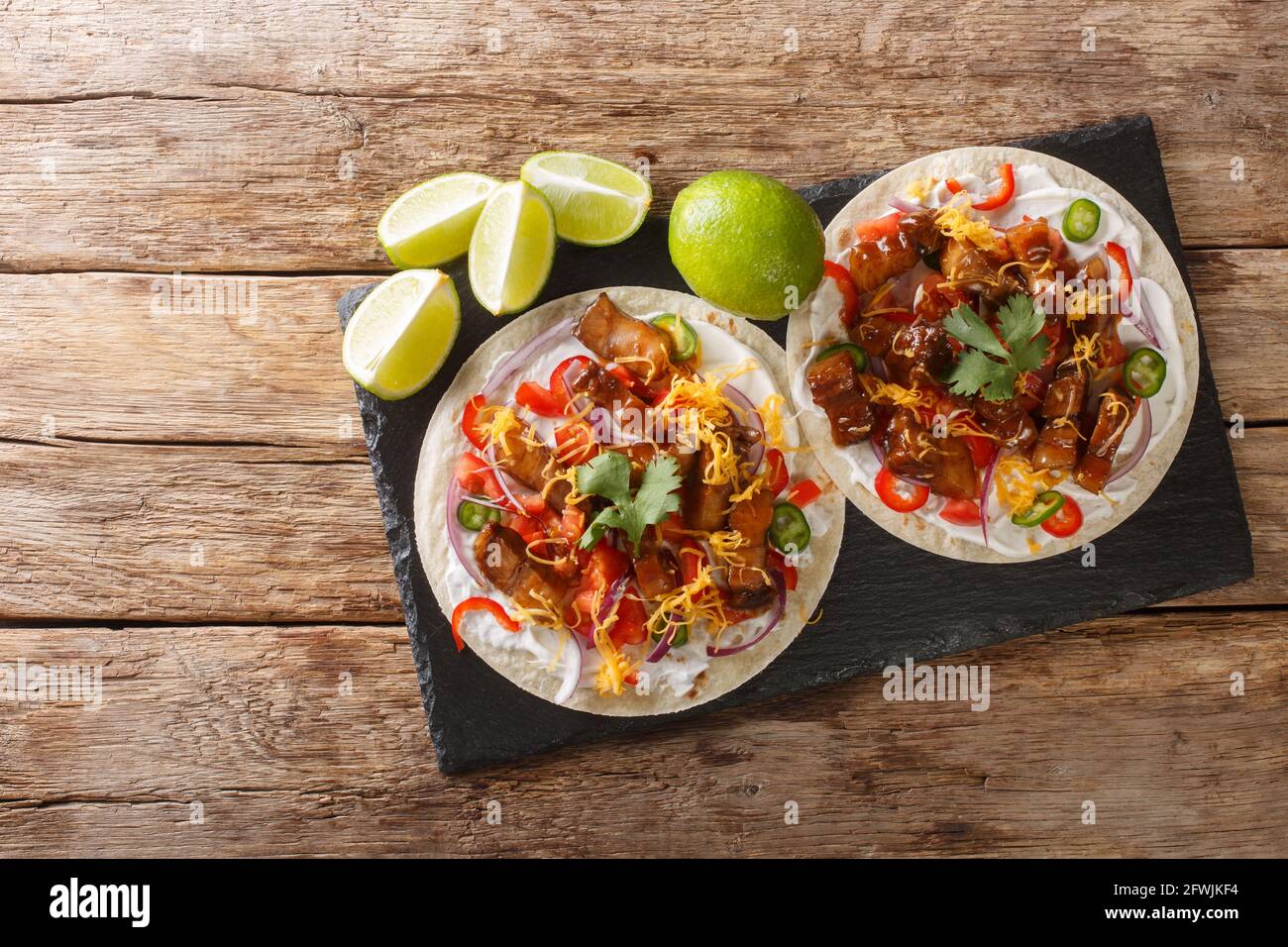 Heiße Tacos mit gegrilltem Schweinebauch, Gemüse der Saison, Cheddar und Limette aus nächster Nähe auf einem Schieferbrett auf dem Tisch. Horizontale Draufsicht von oben Stockfoto