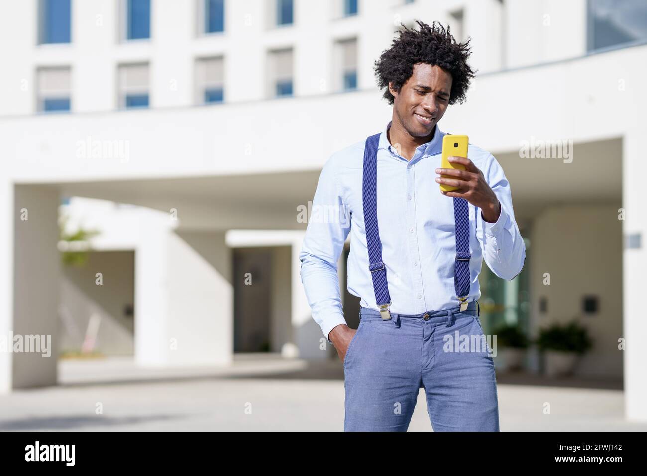 Schwarzer Mann mit Afro-Frisur mit einem Smartphone in der Nähe eines Bürogebäudes. Stockfoto