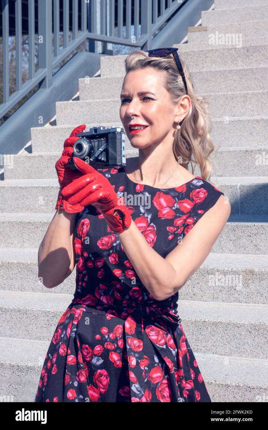 Elegante blonde Frau in einem roten Kleid mit Vintage-Kamera Draußen stehen Stockfoto