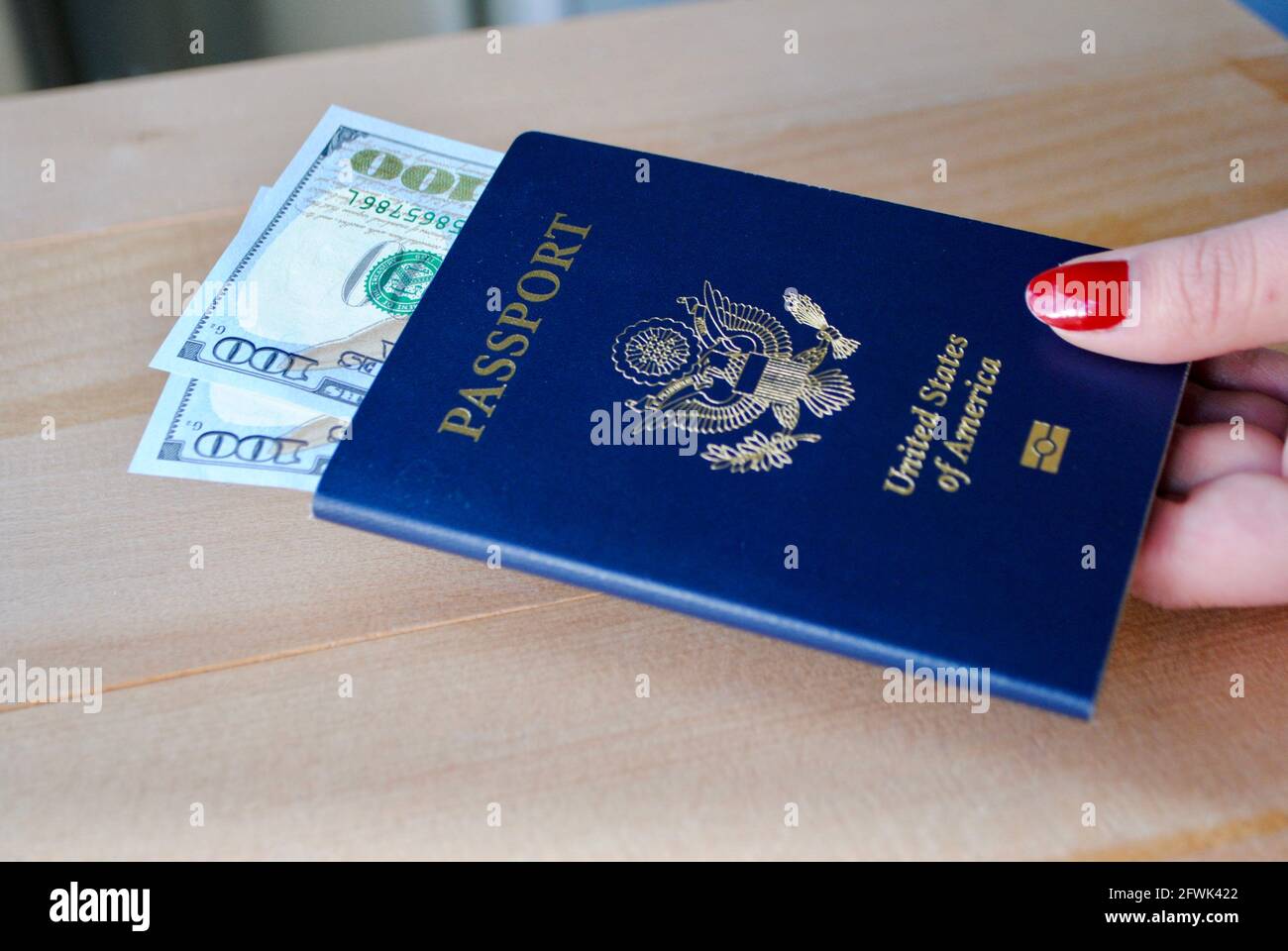 Weibliche Finger mit amerikanischem Pass und Dollarscheinen auf Holzhintergrund. Reisekonzept. Stockfoto