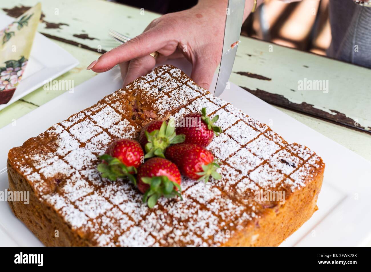 Lady schneidet Kuchen mit Puderzucker und Erdbeeren darauf Stockfoto