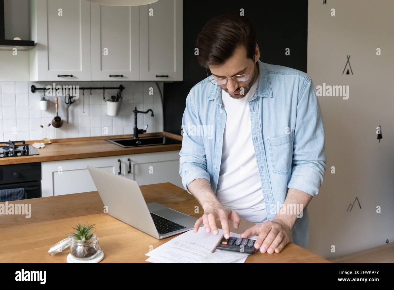 Konzentrierter tausendjähriger Mann, der das monatliche Budget in der Küche plant. Stockfoto