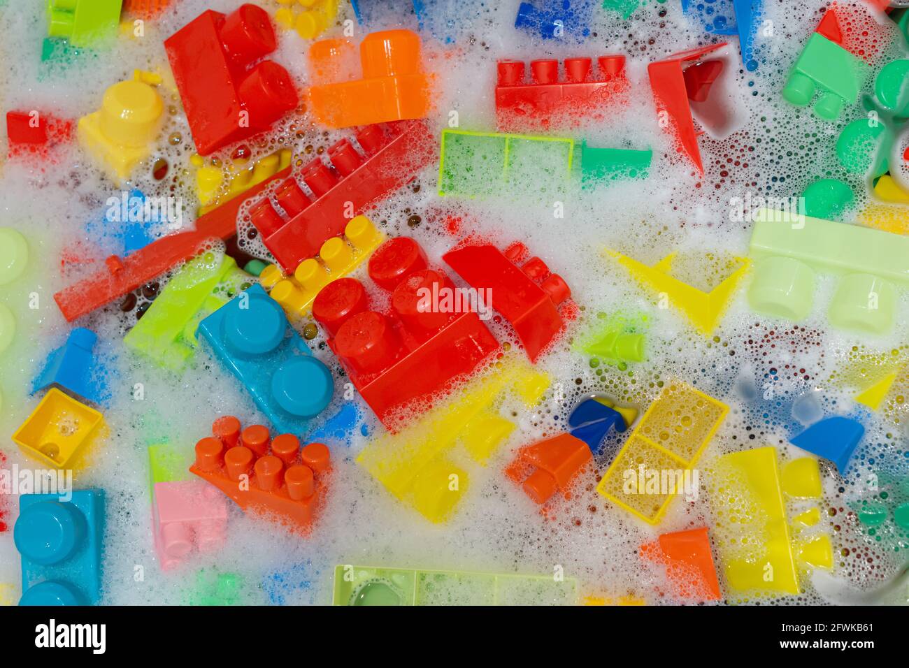 Reinigung von bunten Spielzeugbausteinen. Spielzeughygiene. Waschen von Plastikspielzeug im Bad mit Schaum. Stockfoto