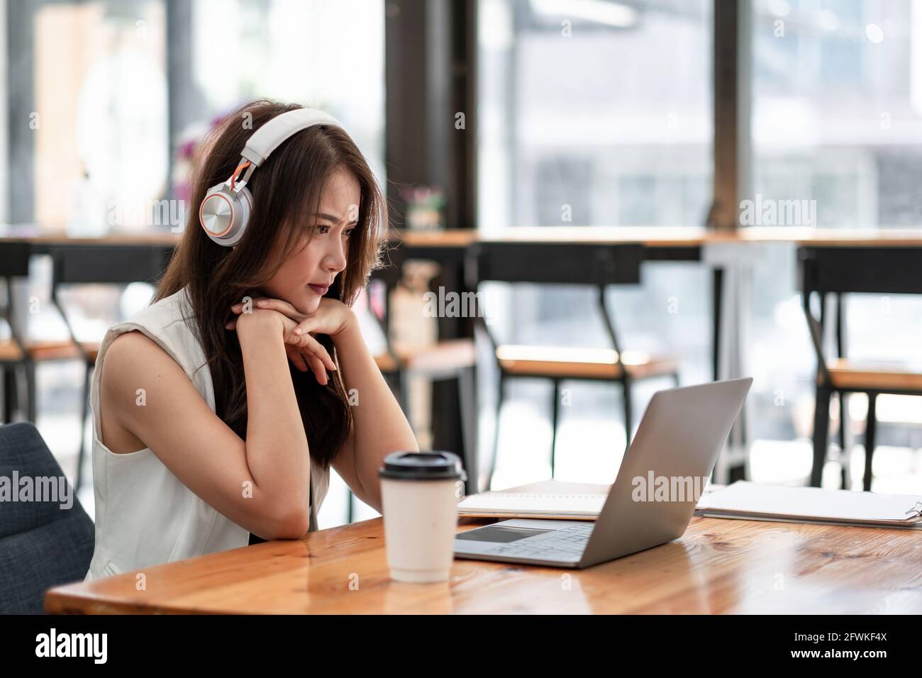 Konzentrierte junge asiatische Frau trägt Kopfhörer Blick auf Laptop für Online-Studie, attraktive weibliche Studenten, die Sprache zu lernen, beobachten online Stockfoto