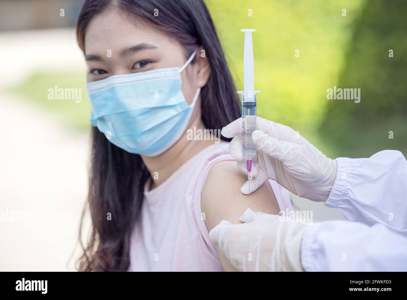 Ärztin mit Spritze, die eine Impfdosis von 19 Covid in der Schulter einer Patientin mit Maske macht. Grippe Influenza-Impfstoff klinisch tr Stockfoto