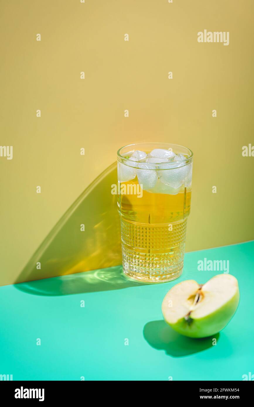 Glas Apfelsaft mit Eis auf gelbem Hintergrund, helle Schatten Stockfoto